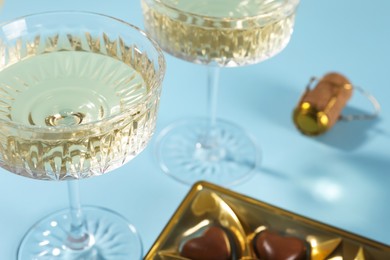 Photo of Glasses of expensive white wine and heart shaped chocolate candies on light blue background, closeup