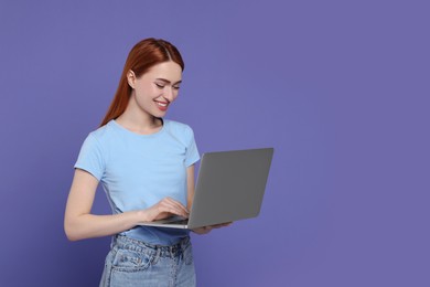 Smiling young woman working with laptop on lilac background, space for text