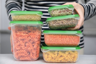 Woman with plastic containers filled of food products at light table indoors, closeup