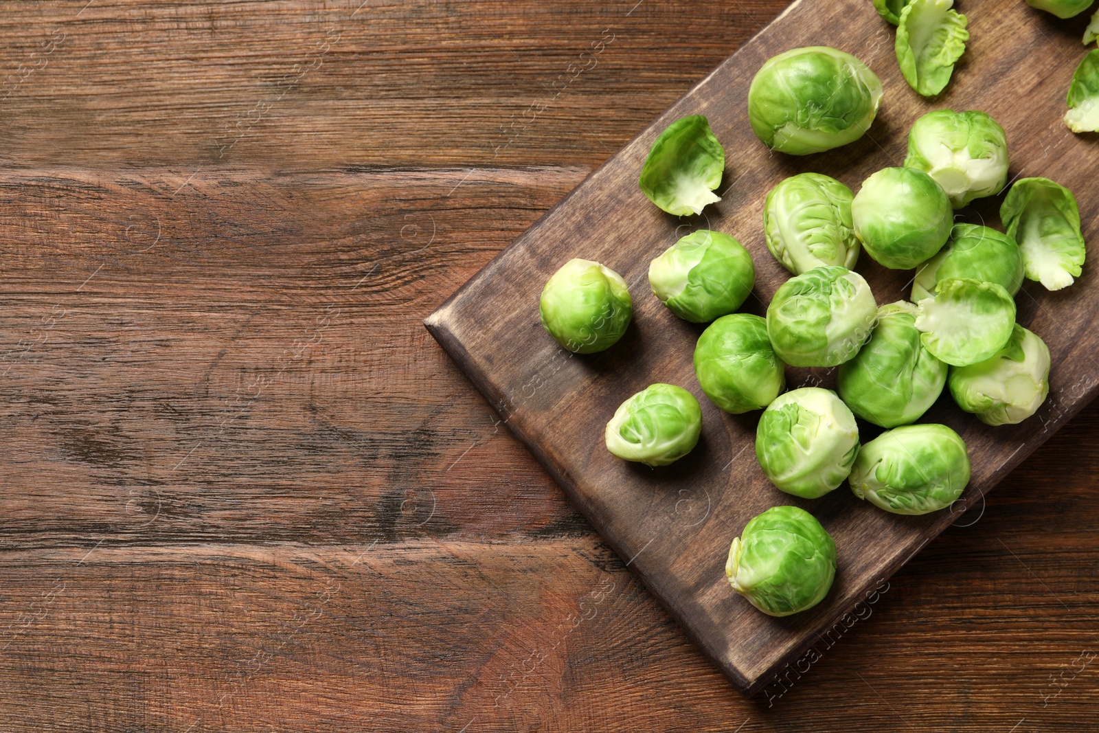 Photo of Board with Brussels sprouts on wooden background, top view. Space for text