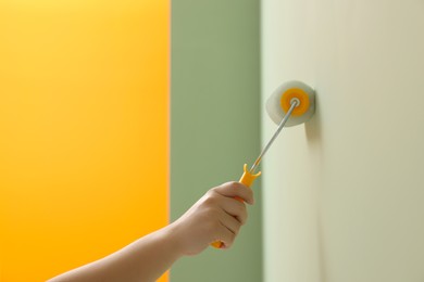 Worker using roller to paint wall with colorful dye indoors, closeup