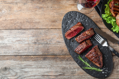 Photo of Delicious sliced beef tenderloin served on wooden table, flat lay. Space for text