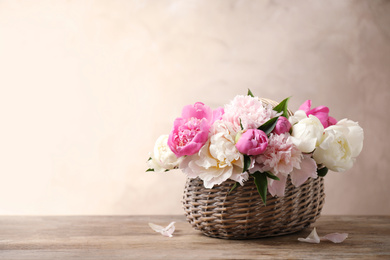 Beautiful peony bouquet in wicker basket on wooden table. Space for text