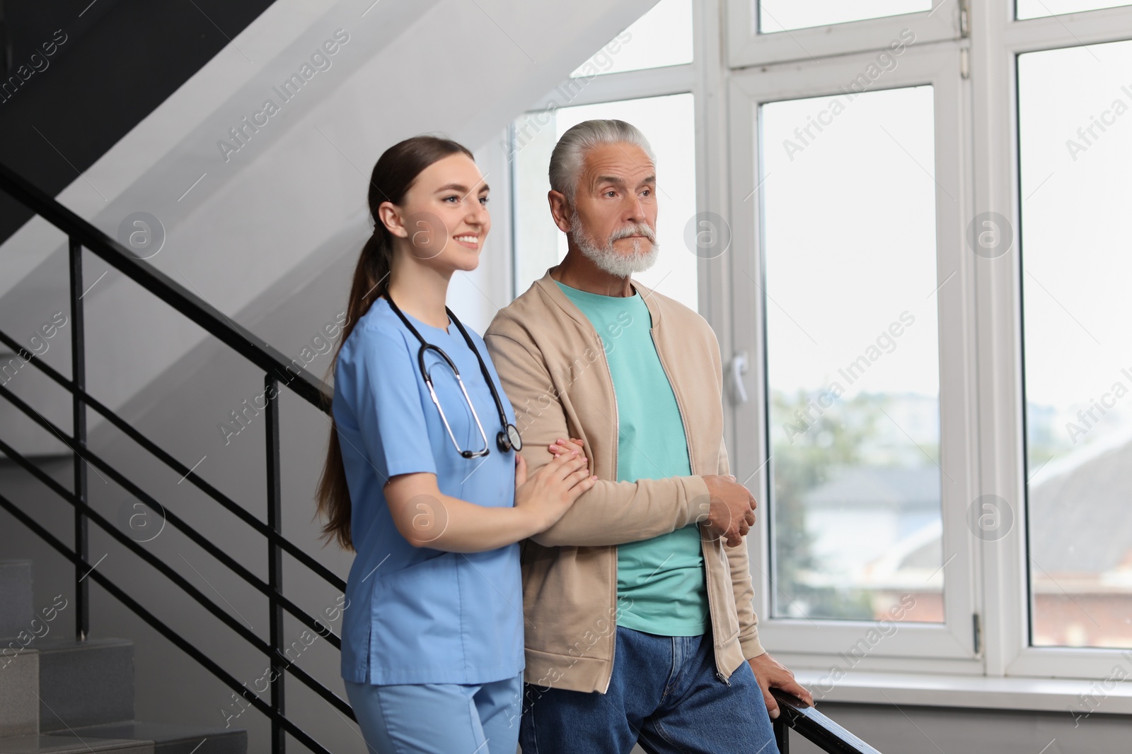 Photo of Young healthcare worker assisting senior man on stairs indoors