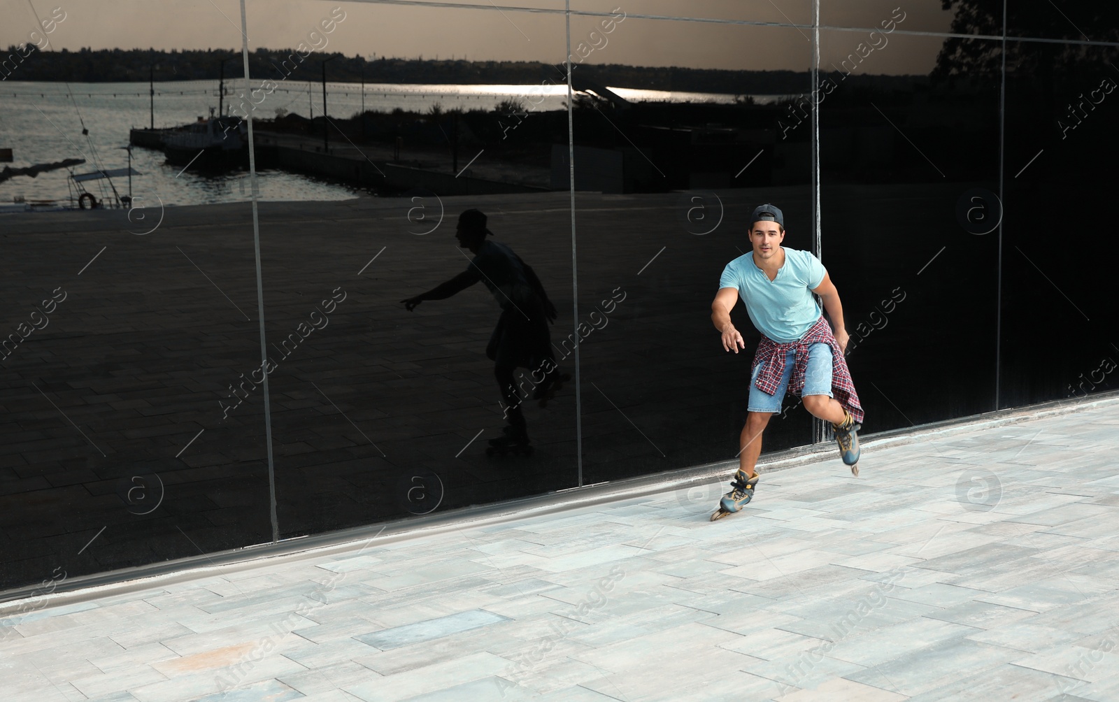 Photo of Handsome young man roller skating near glass building on city street, space for text