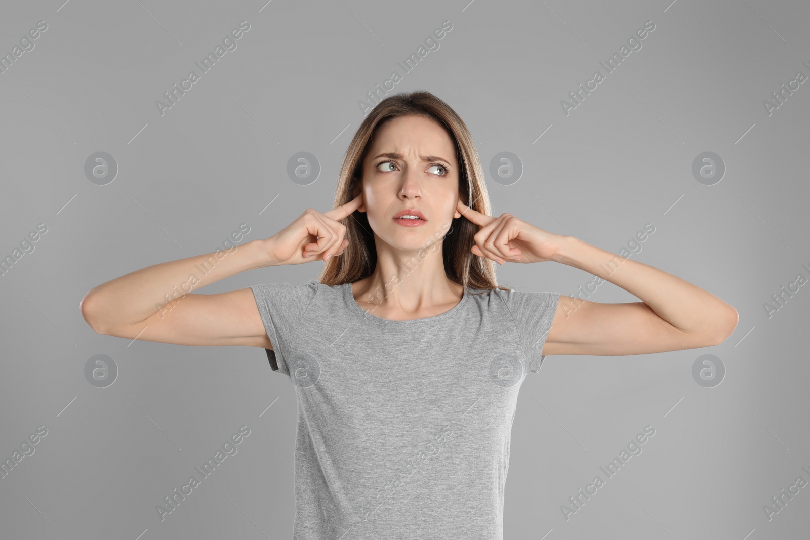 Photo of Emotional young woman covering her ears with fingers on grey background