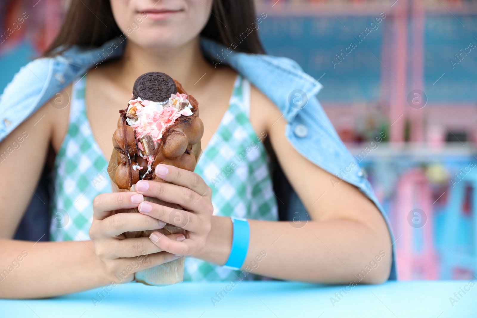 Photo of Young woman holding delicious sweet bubble waffle with ice cream at table outdoors, closeup