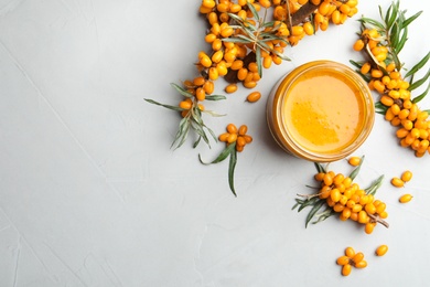 Delicious sea buckthorn jam and fresh berries on light grey table, flat lay. Space for text