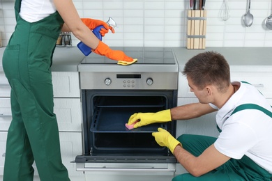 Photo of Team of janitors cleaning kitchen oven in house