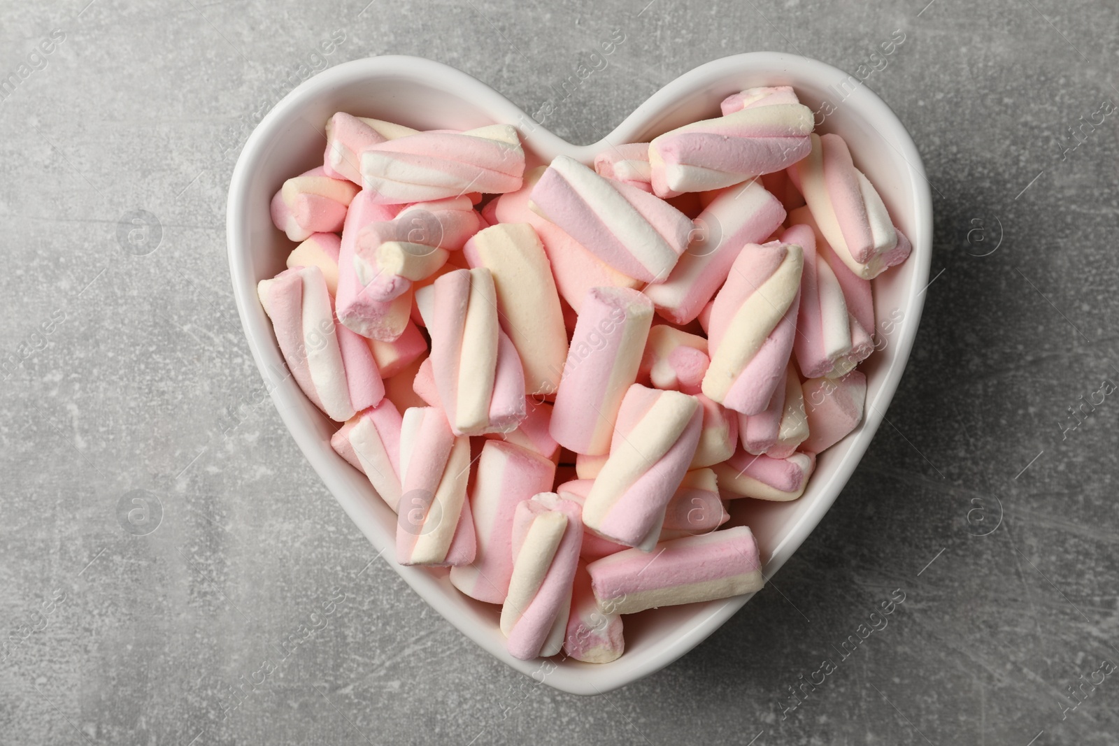Photo of Marshmallows in heart shaped bowl on grey table, top view