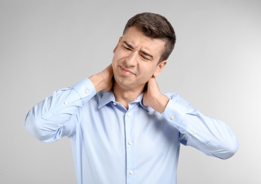 Young man suffering from neck pain on light background