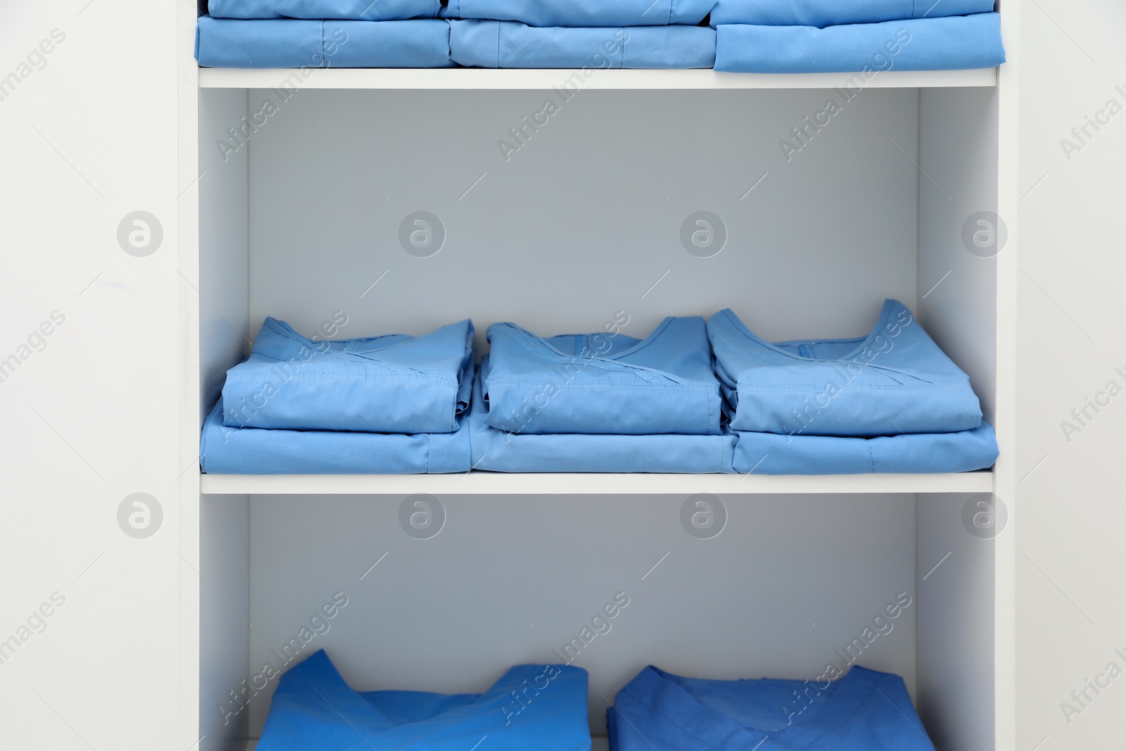 Photo of Light blue medical uniforms on white rack