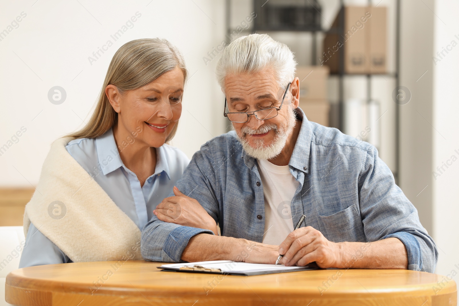 Photo of Smiling senior couple signing Last Will and Testament indoors