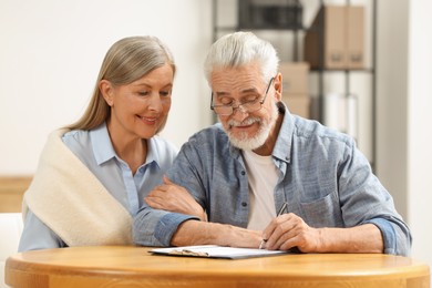 Smiling senior couple signing Last Will and Testament indoors