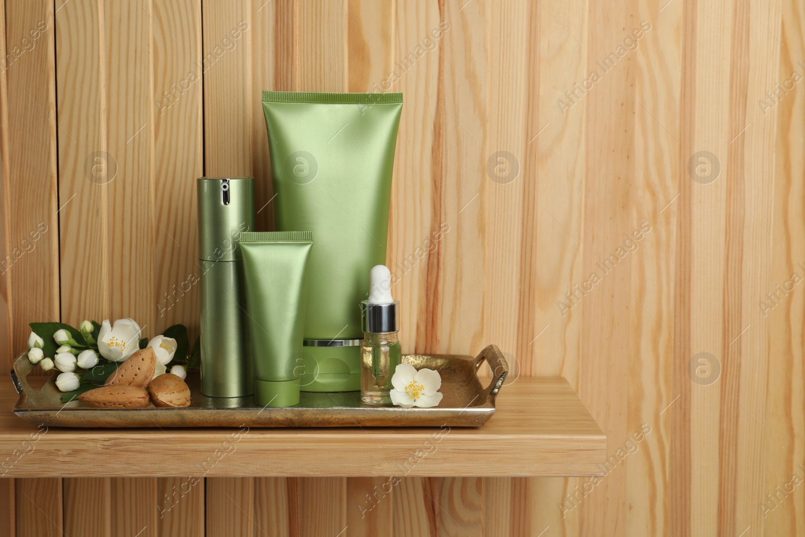 Photo of Set of cosmetic products, almond nuts and flowers on shelf near wooden wall, space for text