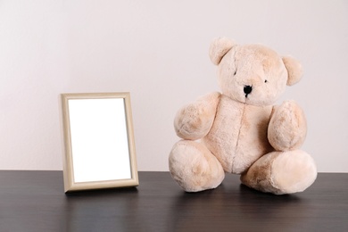 Photo of Photo frame with space for text and adorable teddy bear on table against light background. Child room elements