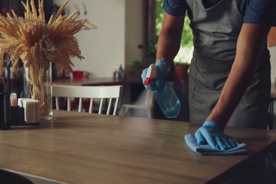 Photo of Waiter in gloves disinfecting table at cafe, closeup