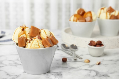 Photo of Delicious ice cream served with caramel and hazelnuts on marble table. Space for text