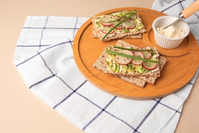 Fresh crunchy crispbreads with cream cheese, radish and green onion on beige table, space for text