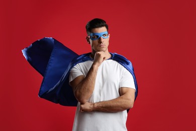 Man wearing superhero cape and mask on red background