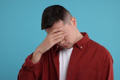 Embarrassed man covering face with hand on light blue background