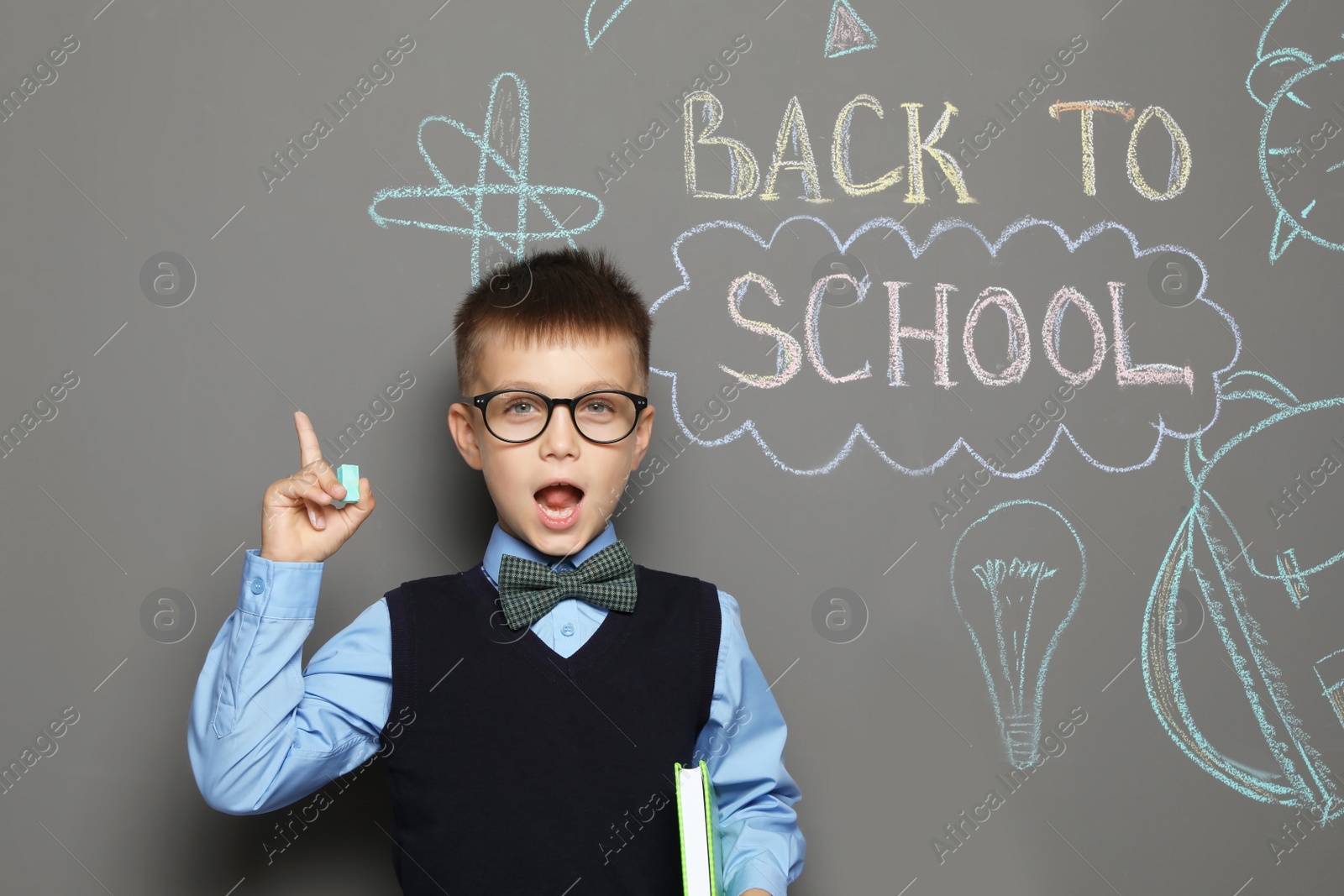 Photo of Little child in uniform near drawings with text BACK TO SCHOOL on grey background