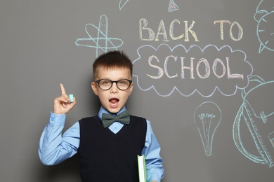 Little child in uniform near drawings with text BACK TO SCHOOL on grey background