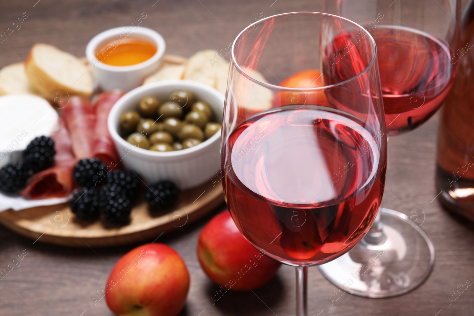 Photo of Delicious rose wine and snacks on wooden table, closeup