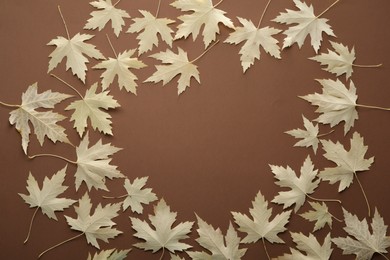 Photo of Frame of dry autumn leaves on brown background, flat lay. Space for text