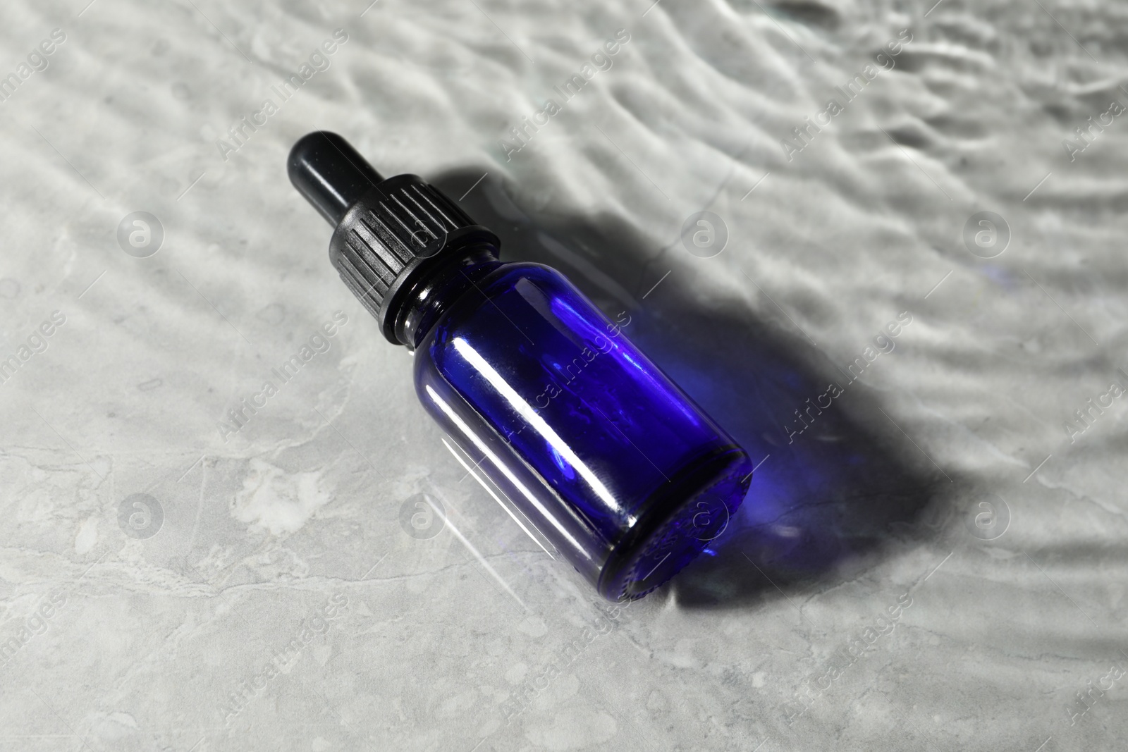 Photo of Bottle of face serum in water on light background
