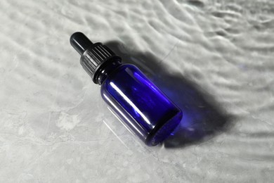 Bottle of face serum in water on light background