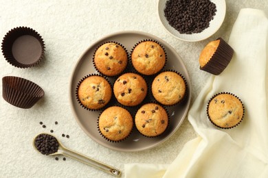 Delicious sweet muffins with chocolate chips on light textured table, flat lay