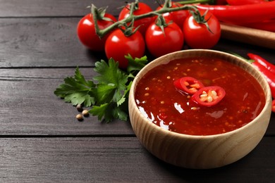 Spicy chili sauce in bowl on wooden table. Space for text