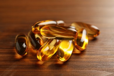 Photo of Dietary supplement capsules on wooden table, closeup