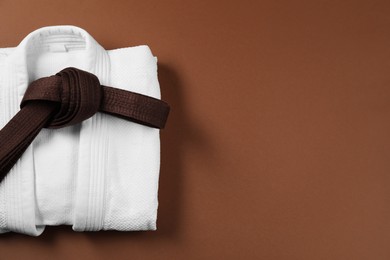 Karate belt and white kimono on brown background, top view. Space for text