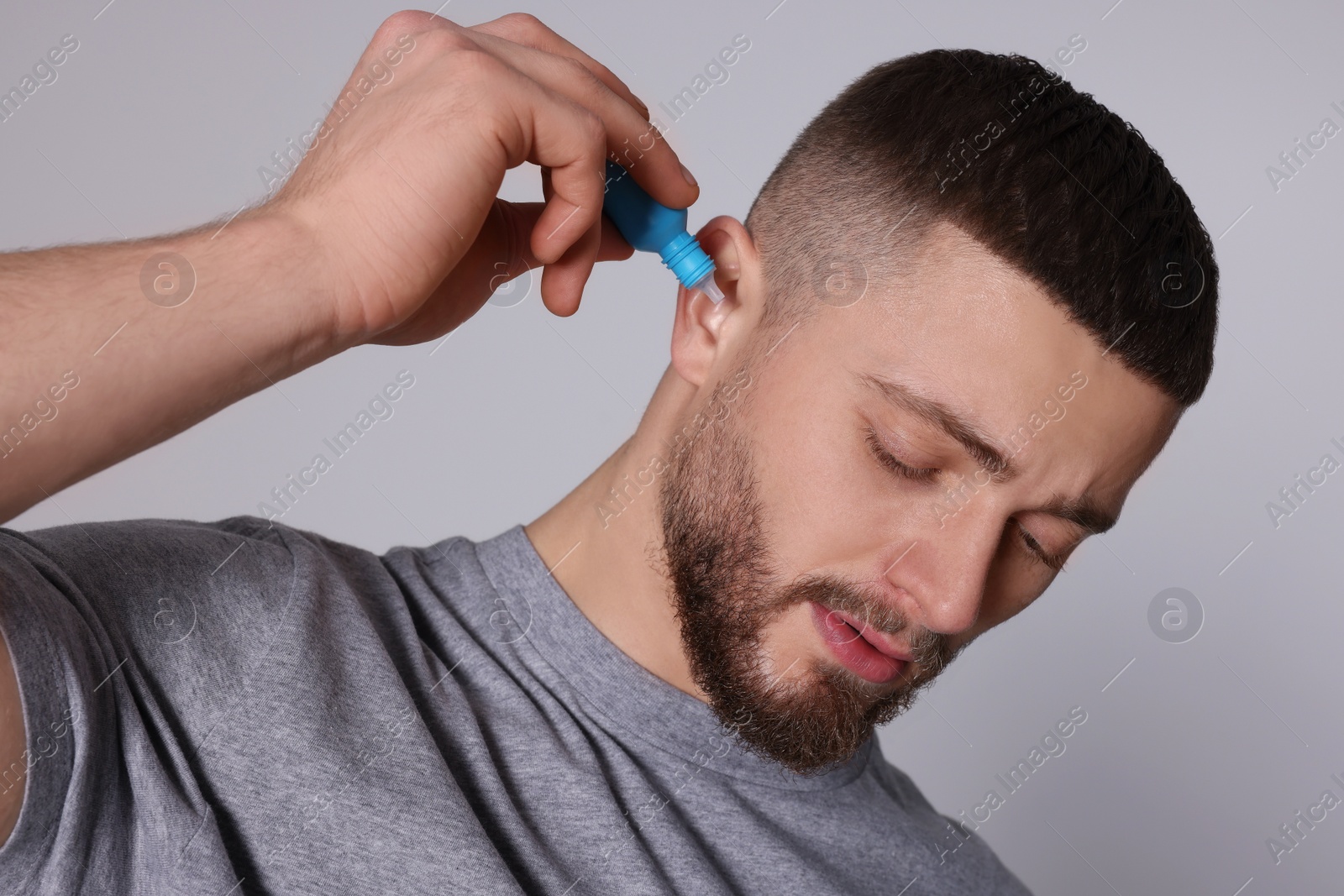 Photo of Man using ear drops on light grey background