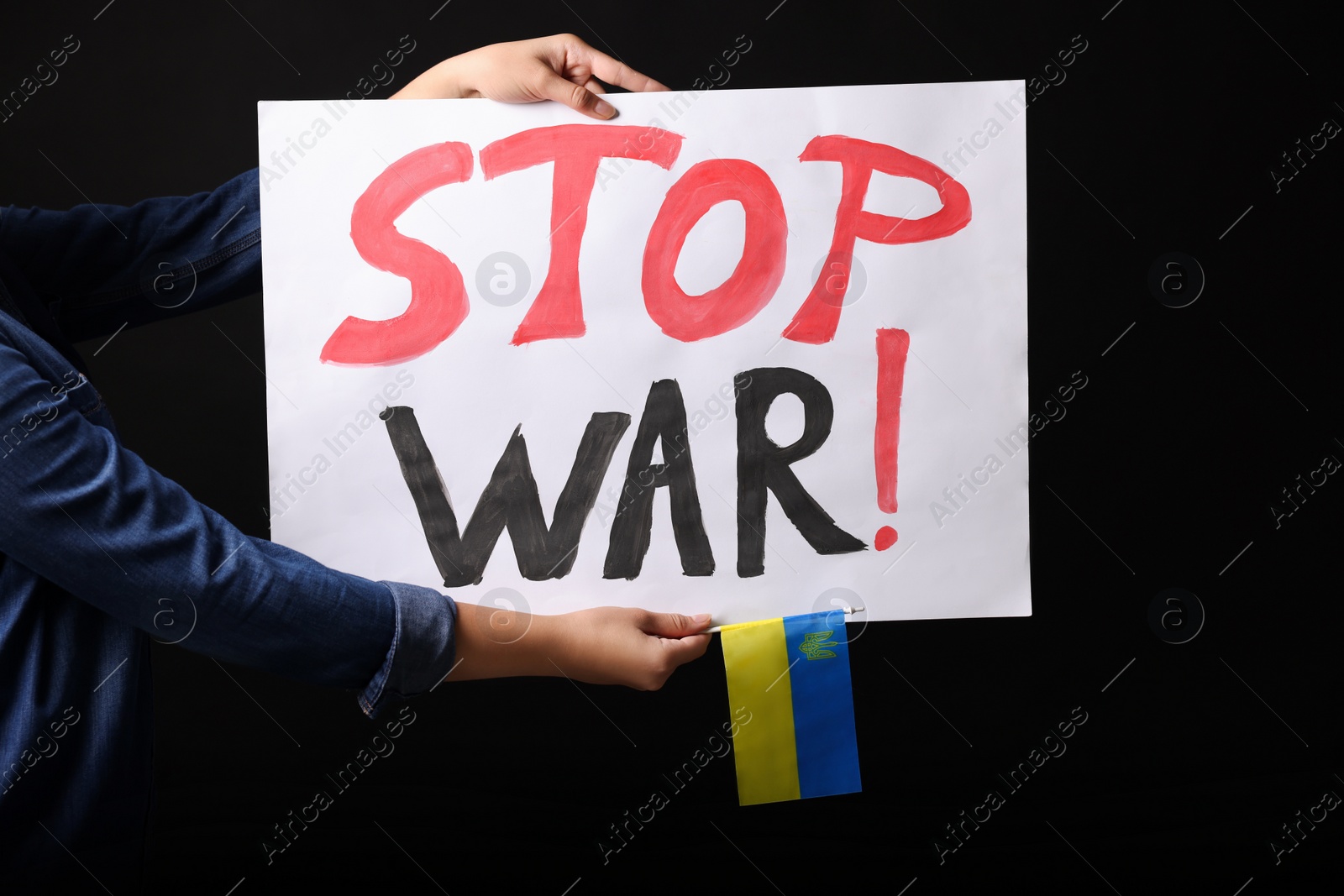 Photo of Woman holding Ukrainian flag and poster with words Stop War on black background, closeup