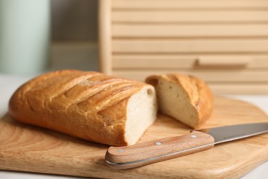 Wooden bread basket, freshly baked loaf on white marble table in kitchen, closeup