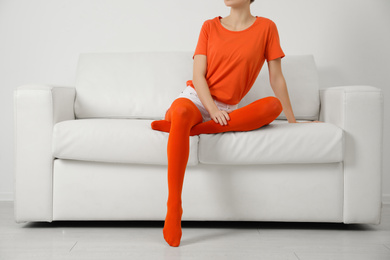 Woman wearing orange tights sitting on sofa indoors, closeup