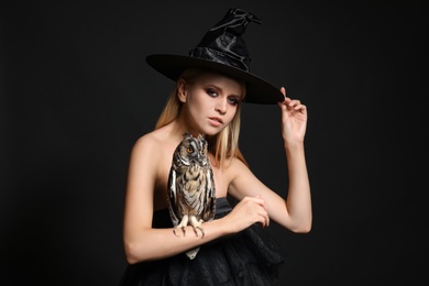 Photo of Witch in black hat with owl on dark background. Scary fantasy character