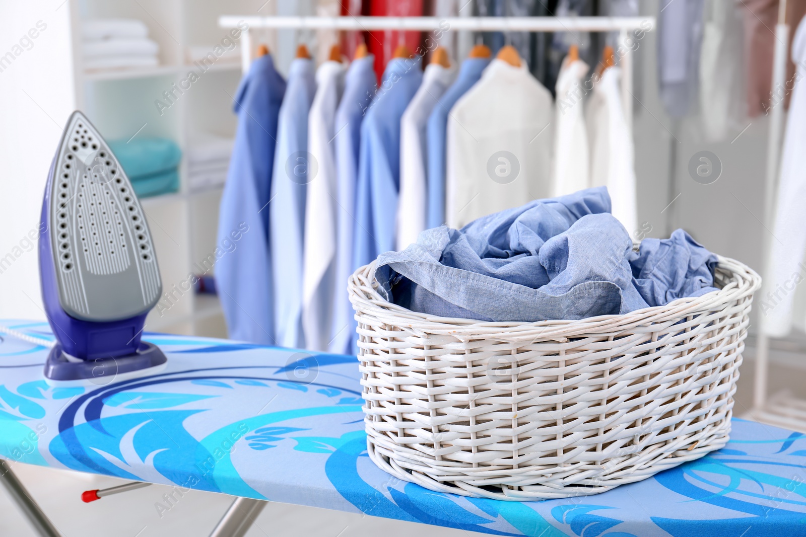 Photo of Wicker basket with clothes on ironing board at dry-cleaner's