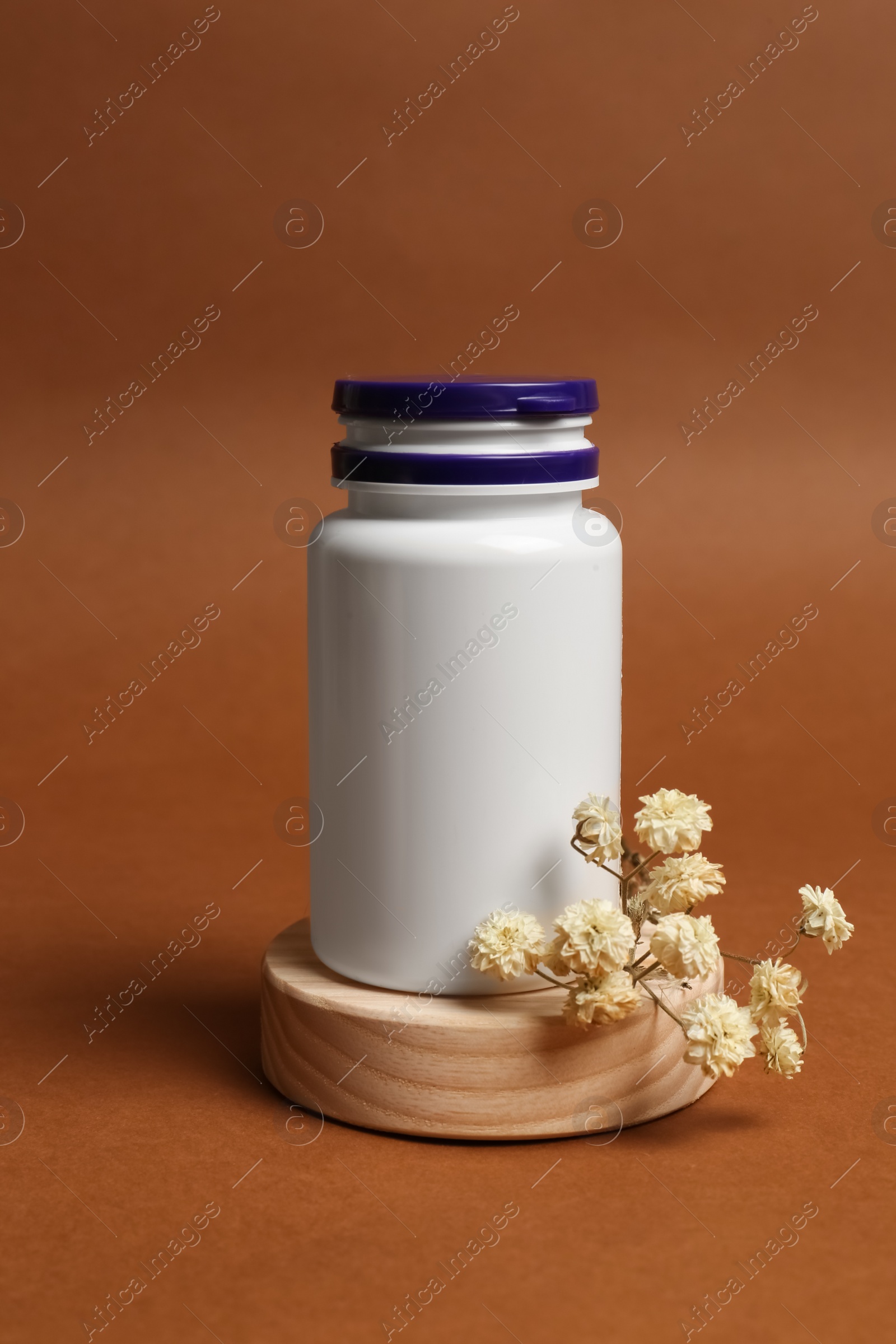 Photo of Medicine bottle near gypsophila flowers on brown background