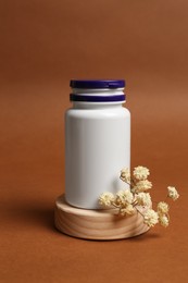 Photo of Medicine bottle near gypsophila flowers on brown background