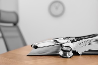 Book and stethoscope on wooden table in clinic. Space for text