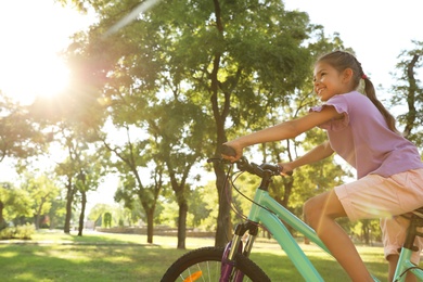 Happy little girl riding bicycle in green park