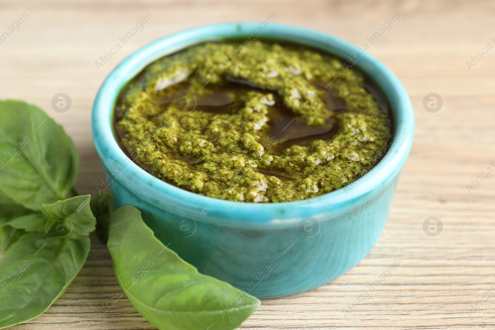 Photo of Tasty pesto sauce in bowl and basil on wooden table, closeup