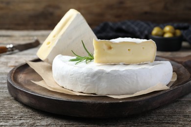 Photo of Tasty cut brie cheese with rosemary on wooden table