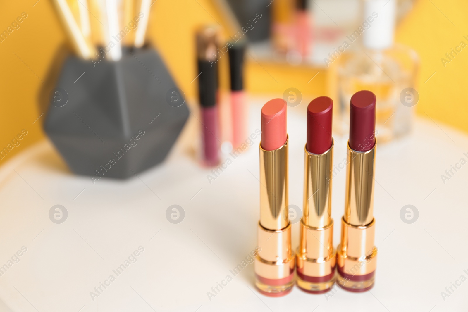 Photo of Bright lipsticks in gold tubes on dressing table, space for text