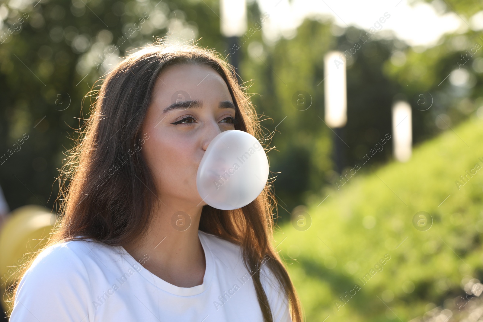 Photo of Beautiful young woman blowing bubble gum in park. Space for text