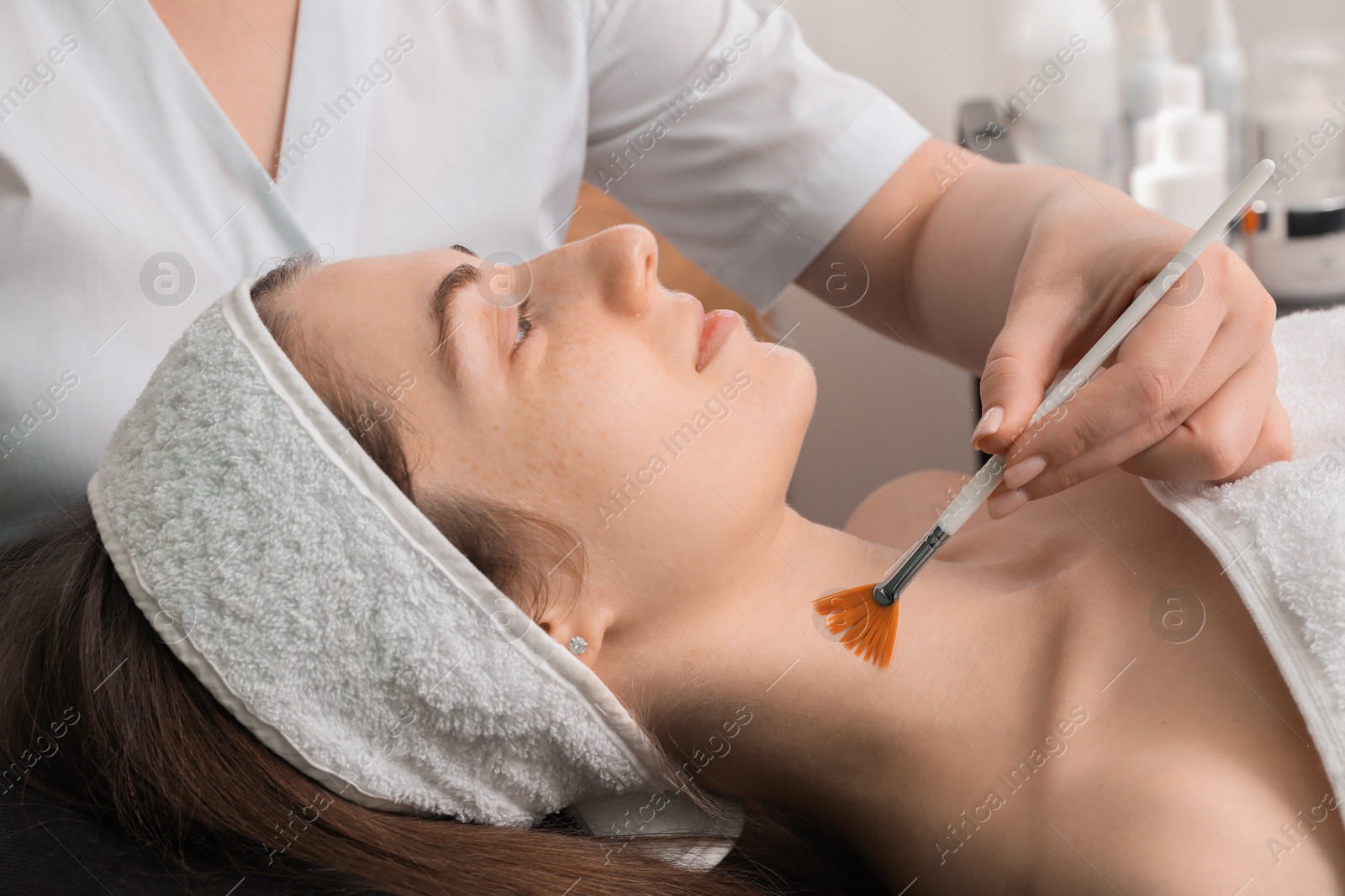 Photo of Cosmetologist with brush applying cosmetic product to client`s neck in clinic, closeup